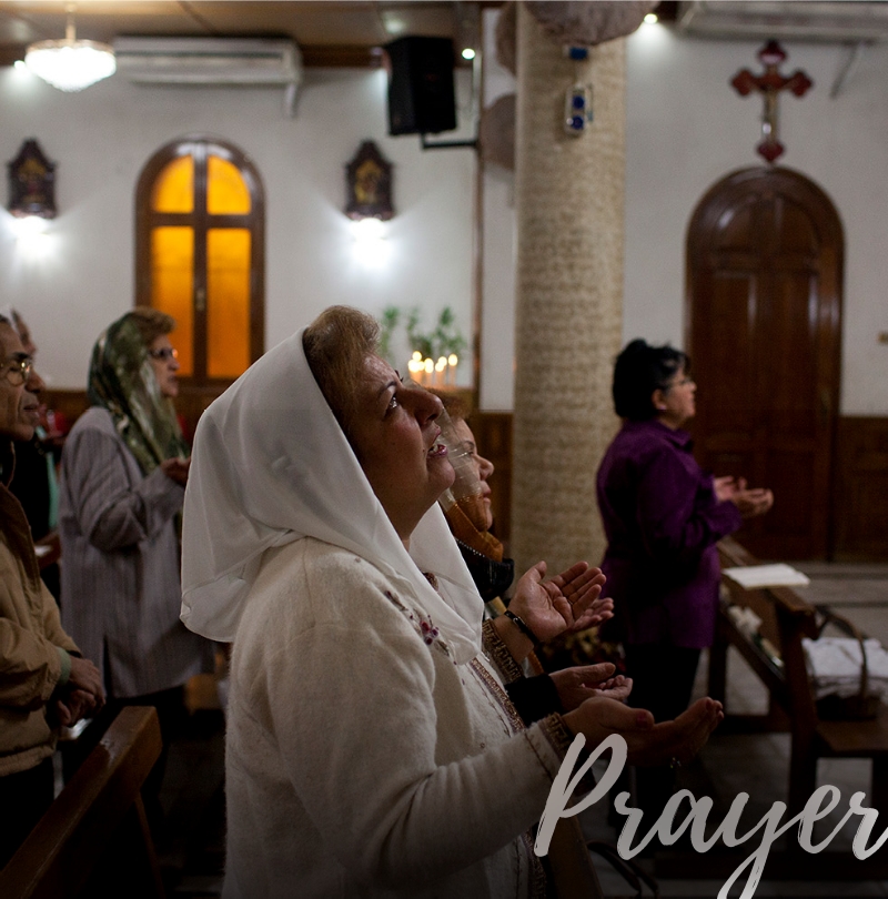 Women kneeling with hands up at their sides praying in pews
